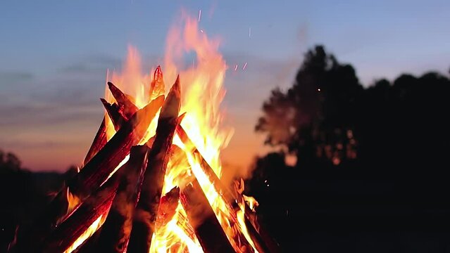 Big Burning Campfire at Summer Evening against the Blue Sky. Wood on Fire. Flying Sparks. Travel and Tourism Concept. Giant Flaming Bonfire - Static Shot, Slow Motion
