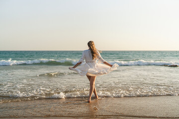 Chica joven en bata blanca de verano entrando en el mar al atardecer 