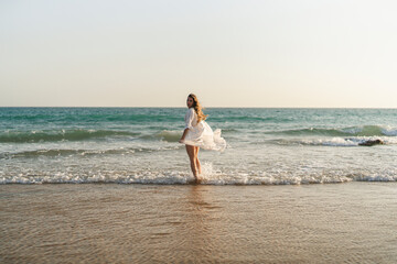 Fototapeta na wymiar Chica joven en bata blanca de verano entrando en el mar al atardecer 