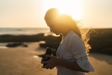 Chica joven al atardecer en la playa haciendo fotos con cámara antigua de carrete de formato medio