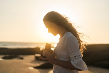 Chica joven al atardecer en la playa haciendo fotos con cámara antigua de carrete de formato medio