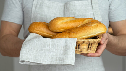 Close up of male hands hold wicker basket with freshly baked french bread baguette and linen towel