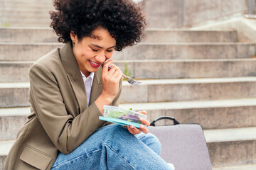 young woman laughing while eating a salad from a lunch box sitting on a staircase during a break...