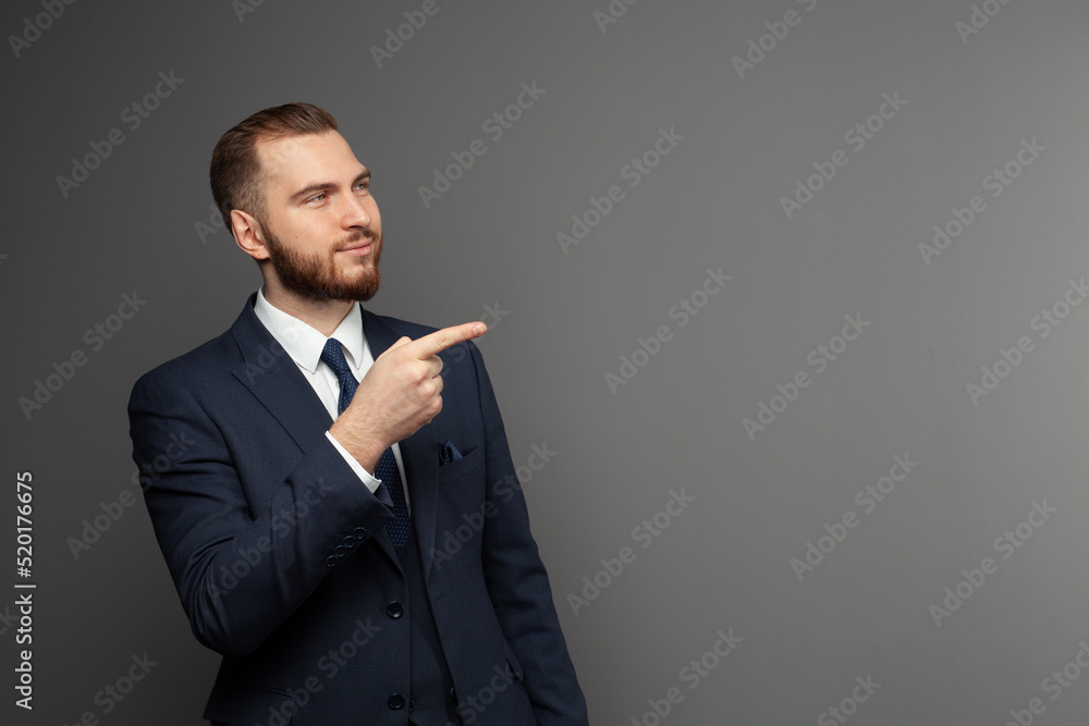 Wall mural successful man wearing suit pointing on a copy space on grey background