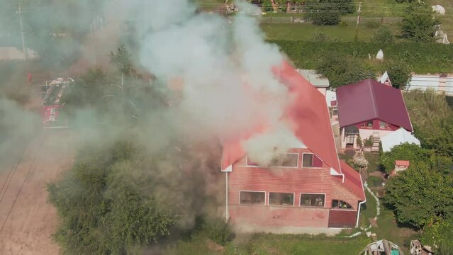 Flight over a burning house. Gray smoke. Fire trucks. Private houses. Emergency. Fire. Aerial drone footage. Top view.