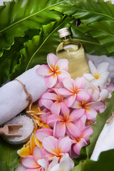 Spa setting with frangipani ,bottles of essential oil, salt in bowl ,rolled towel on big  leaves, 