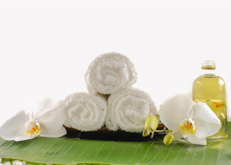 Spa setting with bottles of essential oil , candle , rolled towel, orchid on leaf 