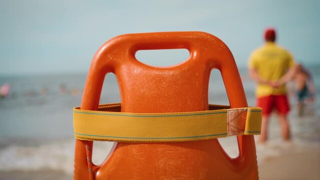 Orange lifeguard buoy with blurred beach rescue worker monitors compliance with rules on beach. Freedom lifestyle and traveling in holiday concept