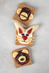 Three sweet toasts for kids in shape of bear, rabbit and monkey, with strawberries, banana, cream cheese, chocolate and coconut flakes on gray background