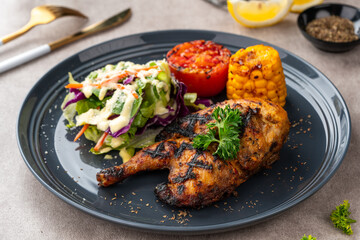 Half chicken baked in a sauce of garlic, soy, ginger, and honey.  plate with baked corn, salad and tomatoes. 