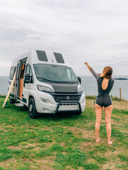 Unrecognizable young woman putting on her wetsuit for surfing next to her camper van