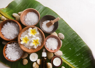 frangipani  in bowl with white salt in wooden bowl ,oil bottle, candle stones with big leaves.