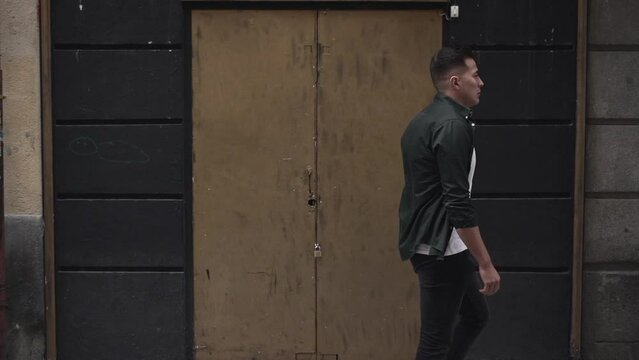 Handsome young man walking down the street in front of a closed door in Madrid. Slow motion. 