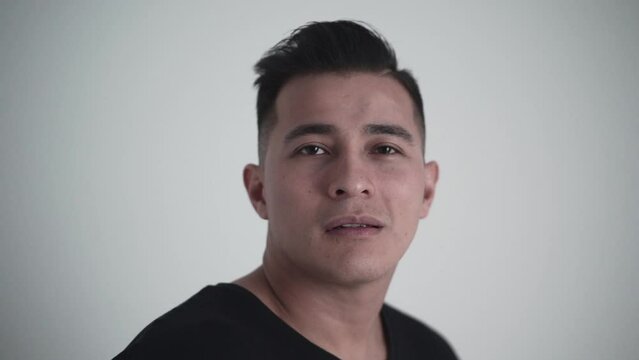 Close up of a young latino posing for the camera holds gaze and then looks up in a white studio
