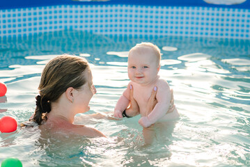 Young mother, swimming instructor and happy little boy in paddling pool. Teaches infant child to swim. Enjoy first day of swimming in water. Mom holds child preparing for diving. doing exercises