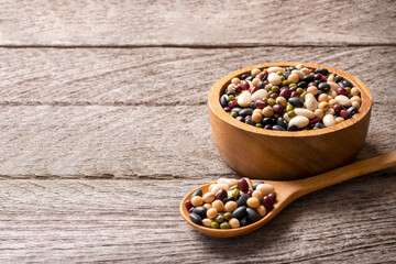 Mix beans in wooden bowl and spoon isolated on wood table background.