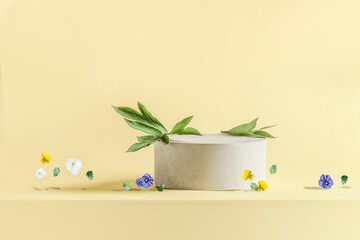 Light yellow product display with cylinder podium, green leaves and flying flowers. Modern floral...