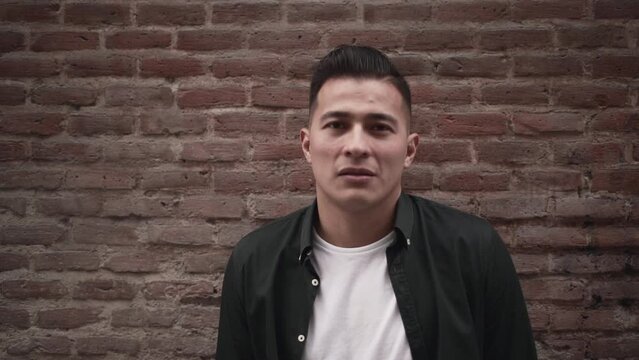Approach of a handsome latino man standing against a brick wall in Madrid