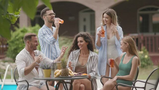 Group of happy young people cheering with cider by the pool in the garden