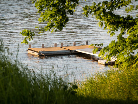 Landing Stage On A River Or A Lake. Natural Area With Many Green Leaves During A Summer Evening. Wooden Planks Swimming On The Water To Moor A Boat Safely. Idyllic Area To Enjoy The Leisure Time.