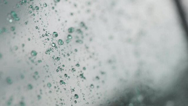 Slow motion handheld shot of rain drops beading on hydrophobic car glass