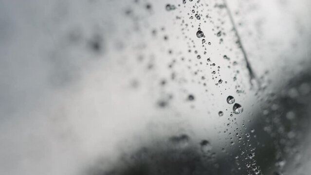 Slow motion handheld shot of rain drops beading on hydrophobic car glass