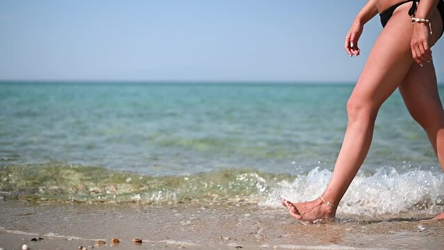 Natural young woman in black bikini bottoms walking along the beach on sunny day