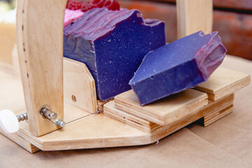 Wooden device for cutting soap handmade with a freshly cut purple bar of soap. Close up
