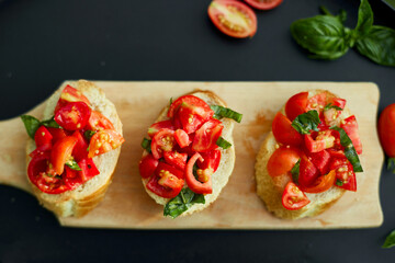 Italian bruschetta with fresh red tomatoes and basil herbs on a wooden board outdoor on the yard, backyard at home, sunlight. Classic Italy food, antipasto