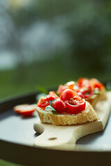 Italian bruschetta with fresh red tomatoes and basil herbs on a wooden board outdoor on the yard, backyard at home, sunlight. Classic Italy food, antipasto