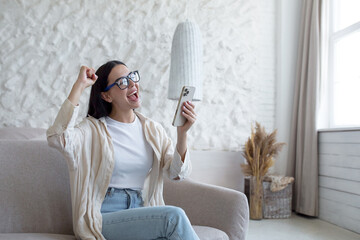 Happy woman at home smiling and happy about received message, brunette sitting on sofa wearing...