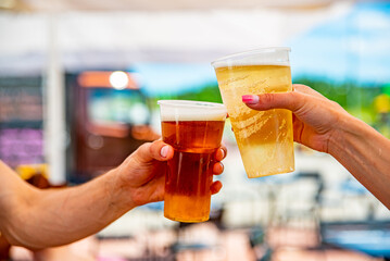 two plastick cup of beer in man and woman hands. Beer clinking outdoor