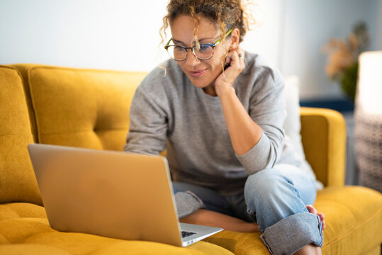 Female sitting on a yellow couch using laptop and internet connection and smile. Happy woman in indoor technology leisure activity. Social media life account concept. Adult Lady writing on computer