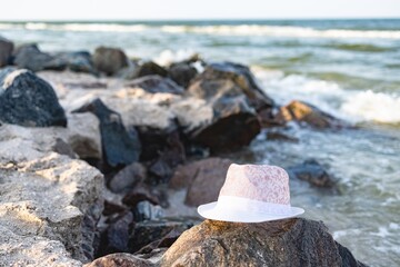 Fototapeta na wymiar The hat lies on the stones near the sea shore under the summer setting sun