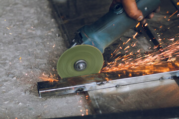 Worker cutting metal frame with hand cutter, disk cutter with sparks