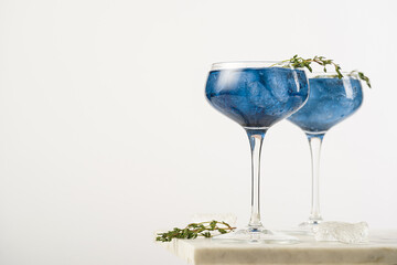 Dark blue drink in a vintage glass for sparkling wine - pea flower tea or blue curacao sirup cocktail with thyme branches on white backgroud. Copy space for text
