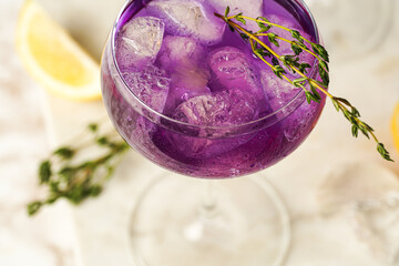 a purple drink in a vintage glass for sparkling wine - pea flower tea or blue curacao sirup cocktail with thyme branches on white background. Top view