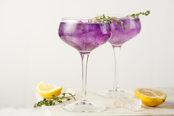 a purple drink in a vintage glass for sparkling wine - pea flower tea or blue curacao sirup cocktail with thyme branches on white background. Copy space for text