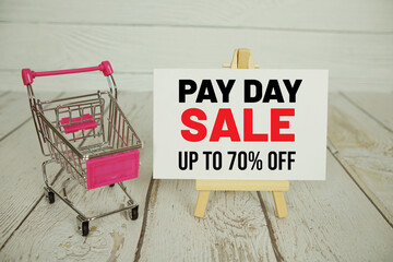 Pay Day Sale text message and shopping trolley cart on wooden background