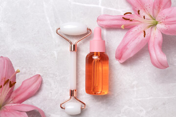 Unbranded serum bottle, face roller with lily flowers on marble background. Face roller for facial massage therapy. Anti age, lifting and toning treatment