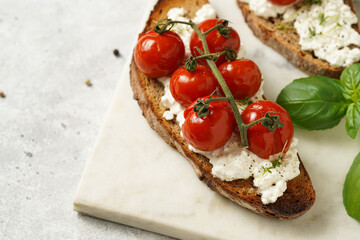 Fototapeta na wymiar A sandwich with roasted cherry tomatoes with branch, fresh cottage cheese, green basil on a slice of whole wheat bread on a marble board on grey background