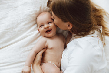 caring and loving mother kissing her little newborn daughter on the bed. mother playing with her...
