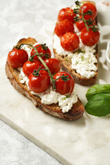 A sandwich with roasted cherry tomatoes with branch, fresh cottage cheese, green basil on a slice of whole wheat bread on a marble board on grey background