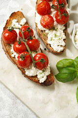 A sandwich with roasted cherry tomatoes with branch, fresh cottage cheese, green basil on a slice of whole wheat bread on a marble board on grey background