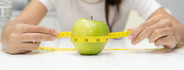 eating healthy and dieting concept. Girl use measure tape measuring green apple on the table.