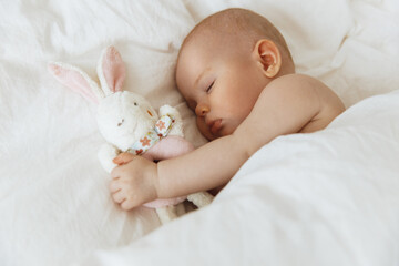 Sleeping little baby with favorite soft toy in hand. Carefree sleep of baby with soft toy on the bed