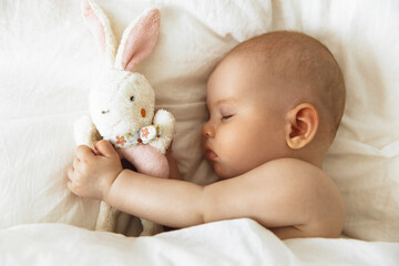 Sleeping little baby with favorite soft toy in hand. Carefree sleep of baby with soft toy on the bed