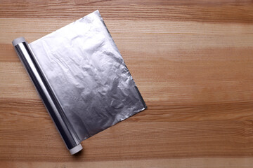 Roll of aluminum foil on wooden table, top view. Space for text