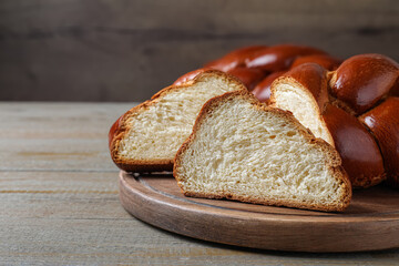 Cut homemade braided bread on wooden table, space for text. Traditional Shabbat challah