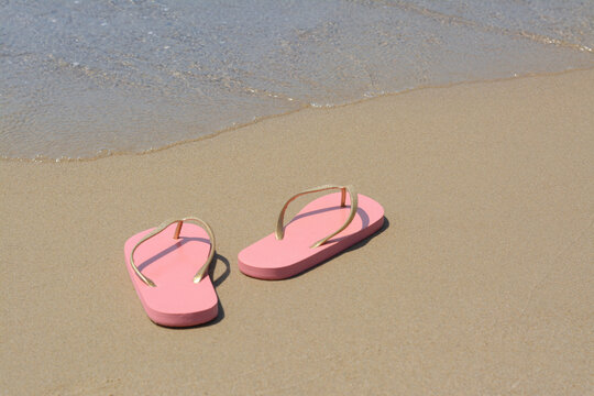 Stylish pink flip flops on wet sand near sea, space for text